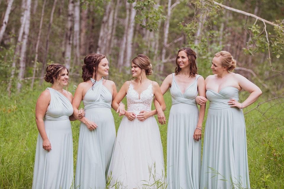 Ashley and her bridal party stand arms linked in a field on her wedding day. Bridesmaids are wearign Henkaa Sakura Convertible Dresses in Mint Green