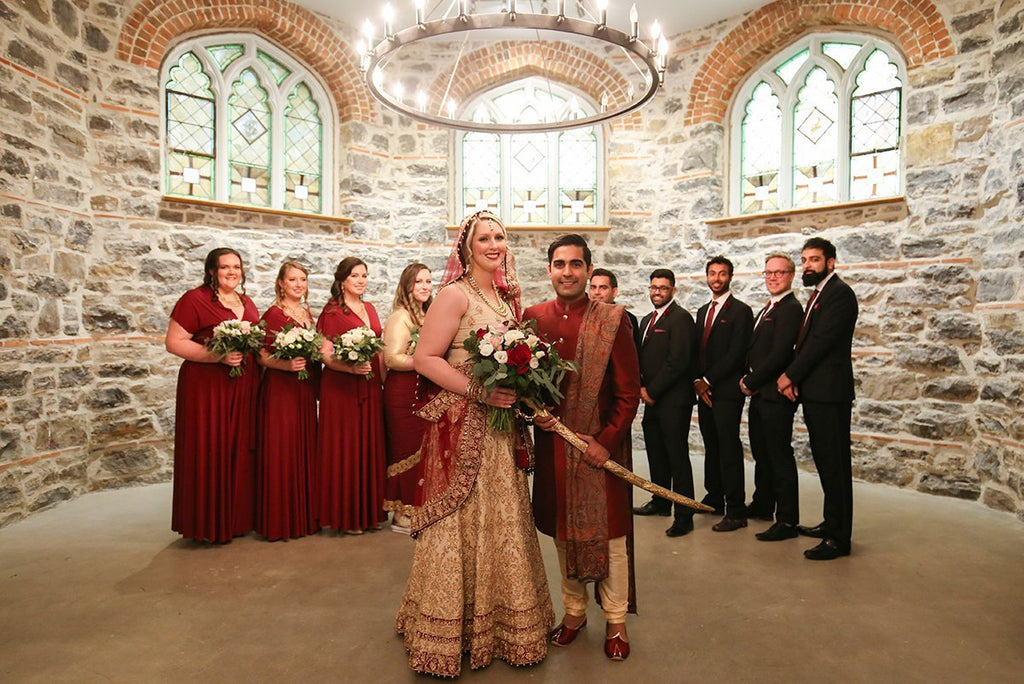 Stephanie and Subhir pose for portraits with their wedding party on their wedding. Brdesmaids are wearing Henkaa Sakura Convertible Bridesmaid Dresses in Burgundy Wine.
