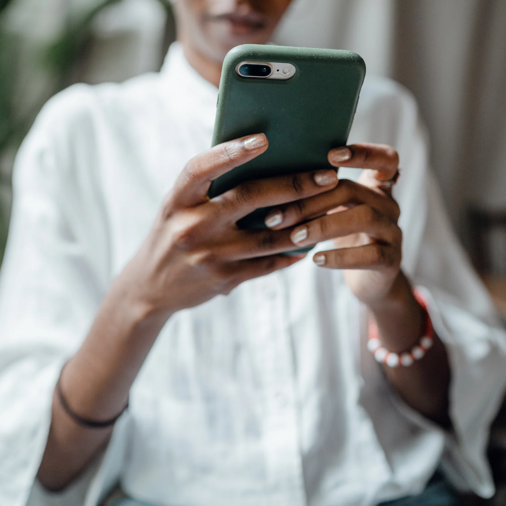 Photograph of a person wearing a white dress shirt and bracelets holding a smartphone that is protected by a green case