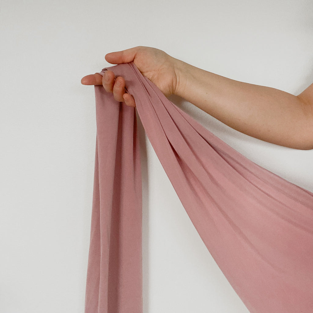 A photo depicts a person's arm holding a long piece of rose-colored fabric