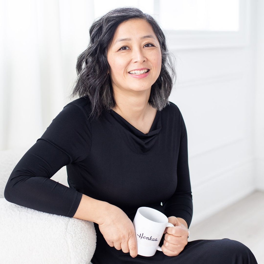 Henkaa co-owner Sonia sitting on couch wearing Iris wrap dress in black and holding a Henkaa coffee mug