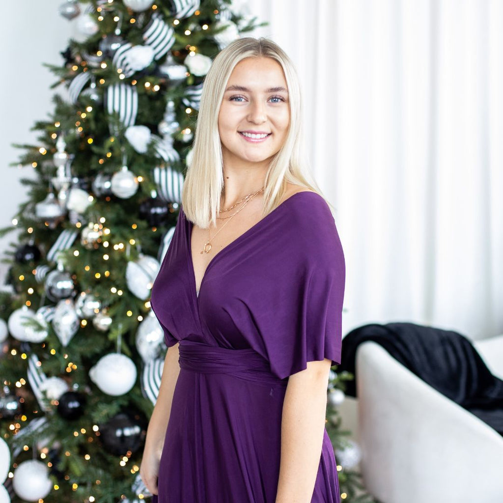 Woman in eggplant purple Sakura maxi standing in front of a Christmas tree