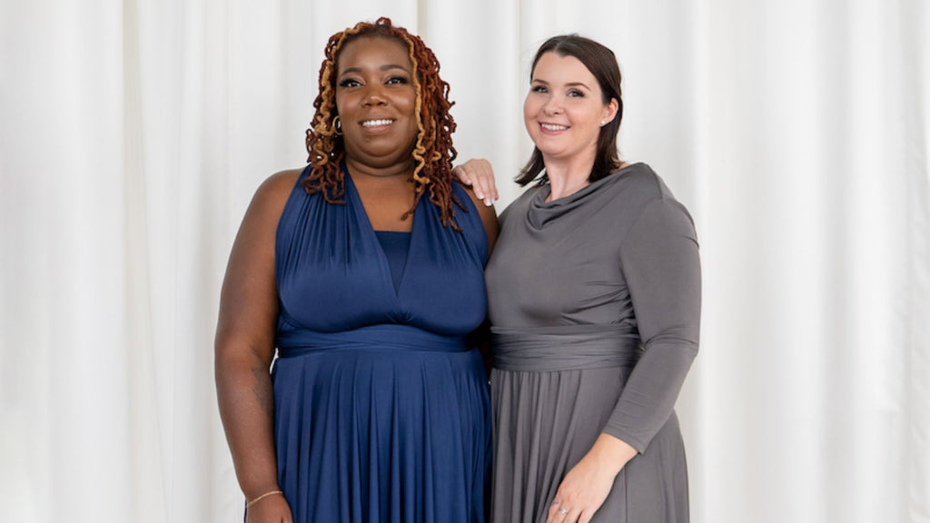 2 women smiling at camera - one is wearing Henkaa Sakura plus size navy dress and one is wearing Iris multiway wrap dress in charcoal grey